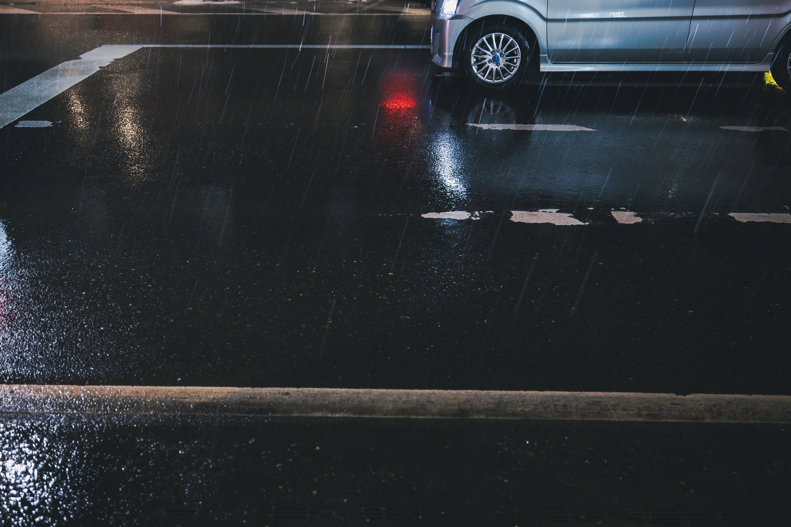 強い雨が降る駐車場にシルバーの自動車が停まっている写真