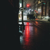 雨天の交差点で赤信号に停止する軽自動車の夜間走行シーンの写真