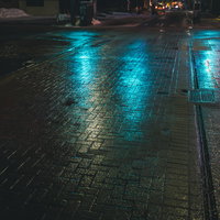 青信号に照らされた雨の夜の交差点、濡れた舗装道路に映る光の写真