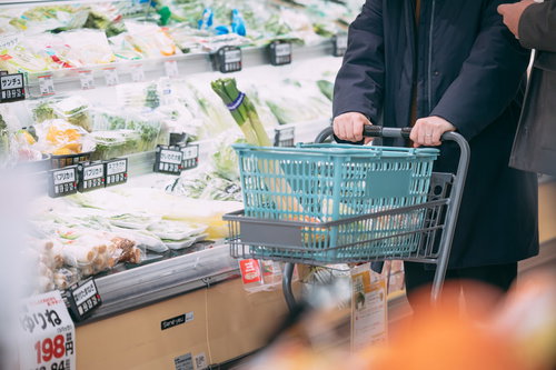 買い物カートを押して青菜などの食材を選ぶ様子