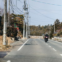 福島県の中通りを走行するバイクと電柱が立ち並ぶ道路の写真