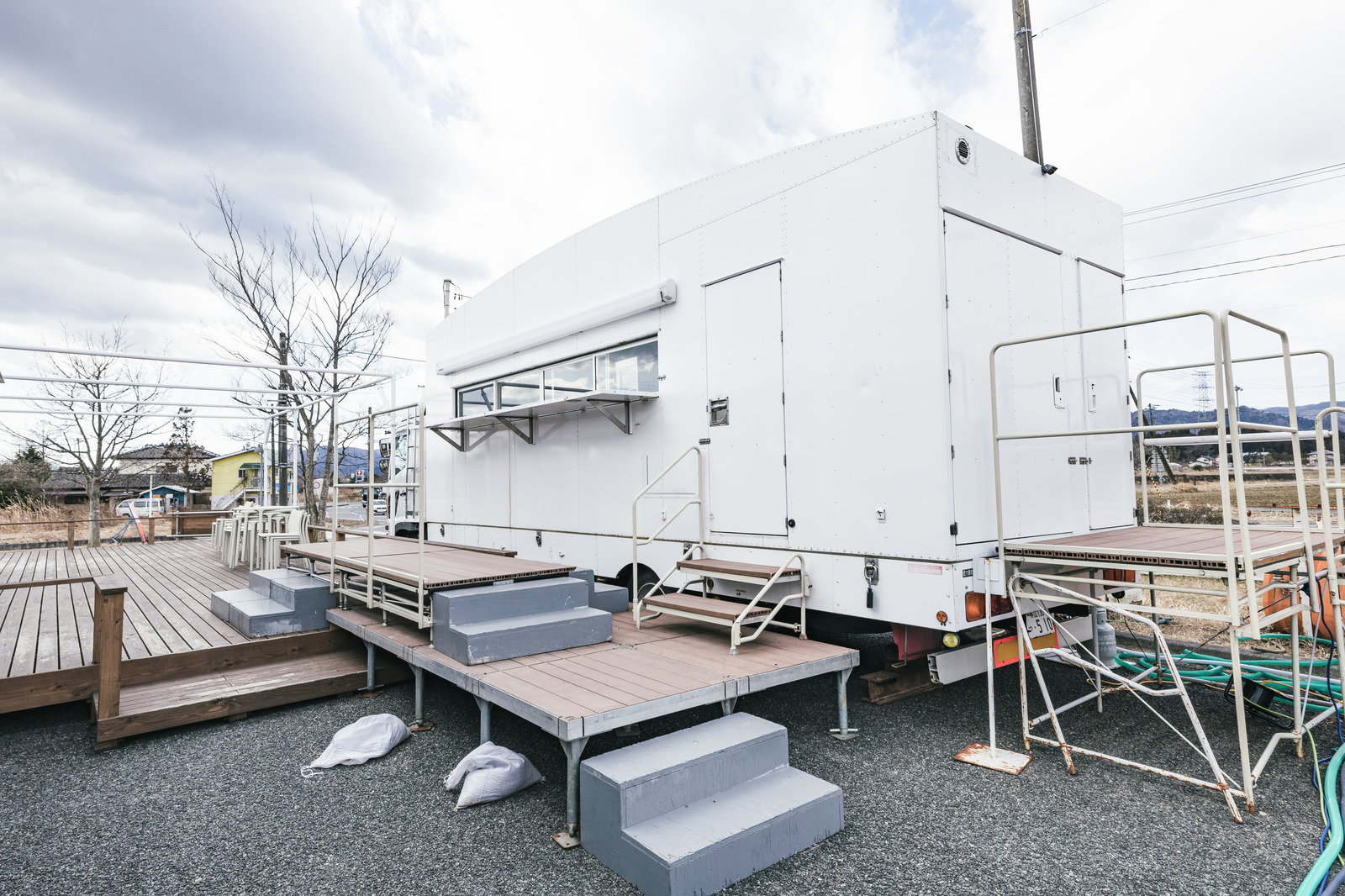 白いキッチンカーの側面、金属製の足場と木製デッキが接続されている