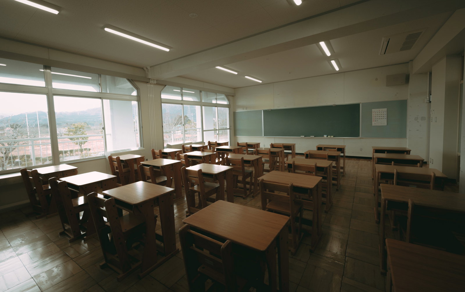 木製の机と椅子が並び、黒板が掛けられた廃校舎の教室