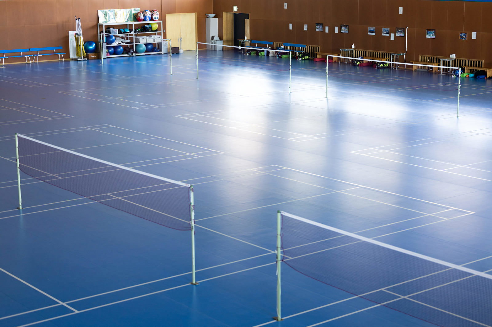 青い床に白線が引かれたバドミントンコートと複数のネットが設置された体育館の室内風景