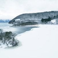 真冬の鬼沼ワンド、雪に覆われた湖畔と山並み（福島県郡山市湖南町）の写真