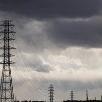 曇り空に並ぶ鉄塔と送電線の写真