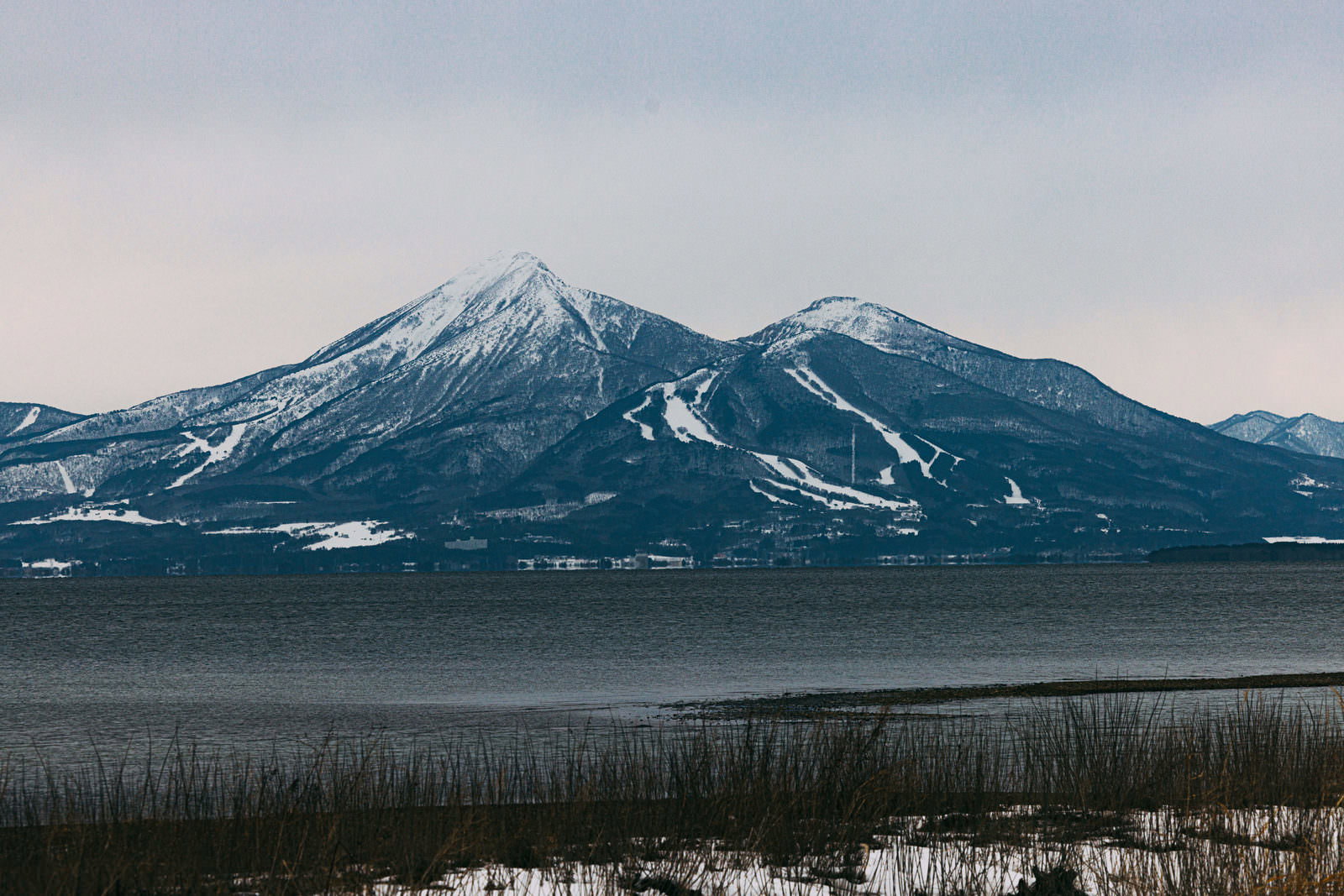 雪が残る2月の磐梯山と猪苗代湖を湖畔から望む風景