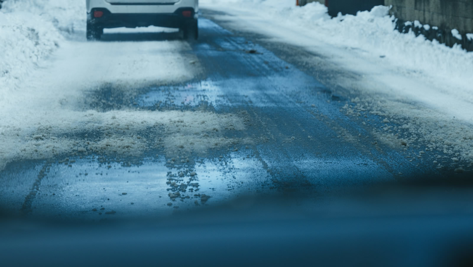 雪が積もったアスファルト路面に融けた水が流れ、アイスバーン状になっている道路と走行する自動車