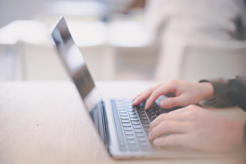 木目のデスクでノートパソコンにタイピング入力する手元