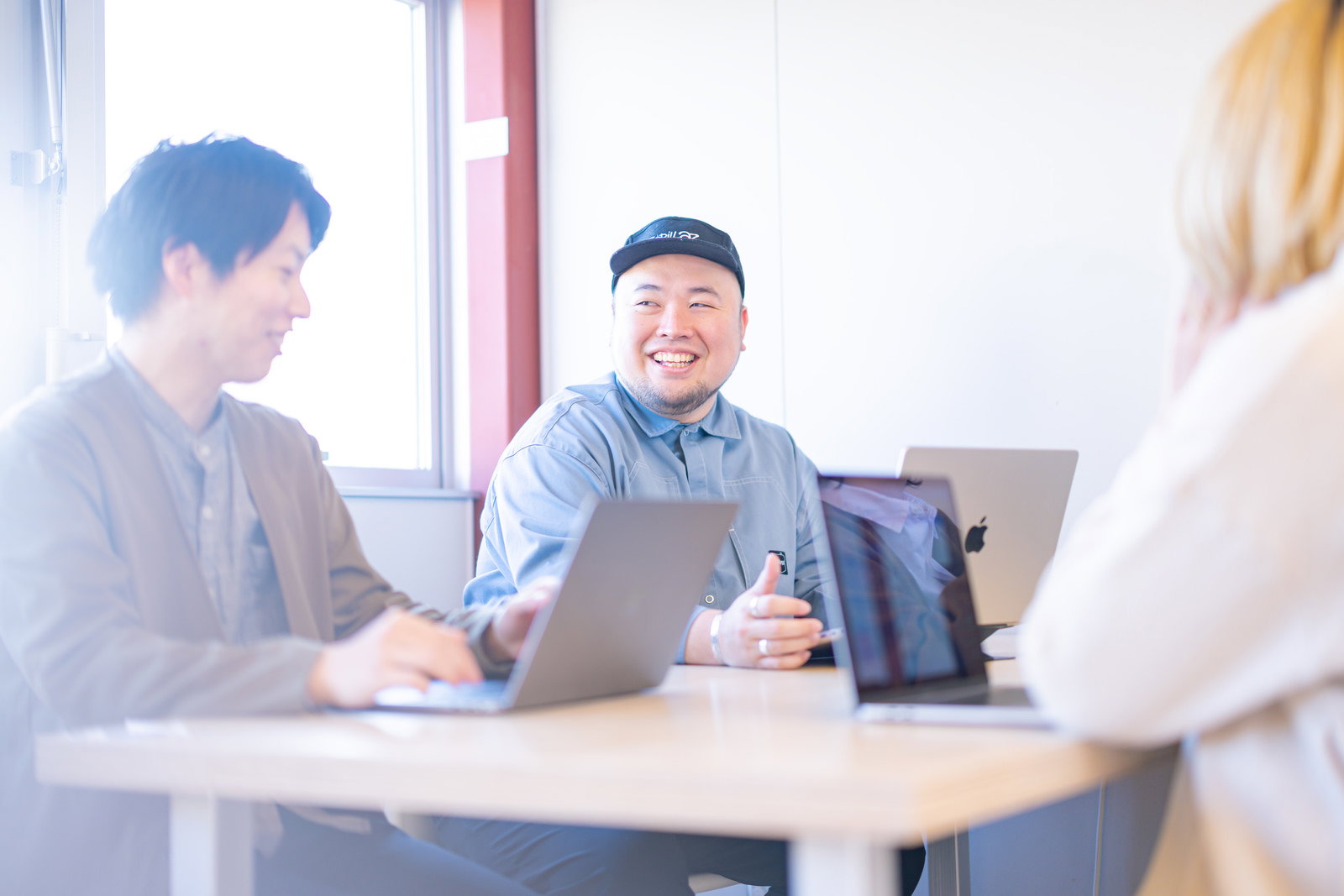 コワーキングスペースで談笑しながら会議をする男性たちとノートパソコン