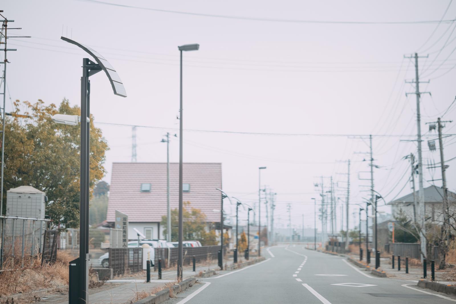 秋の双葉町の道路を走行。街路灯と電柱が並ぶ通りの先に住宅街が見える
