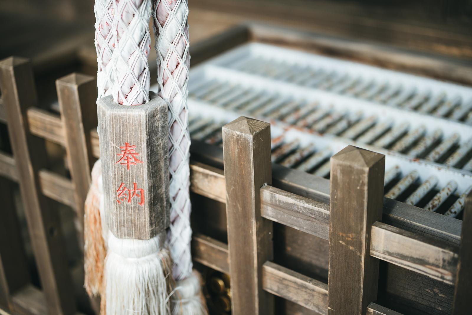 神社の木製賽銭箱に掛けられた白い編み綱と装飾品