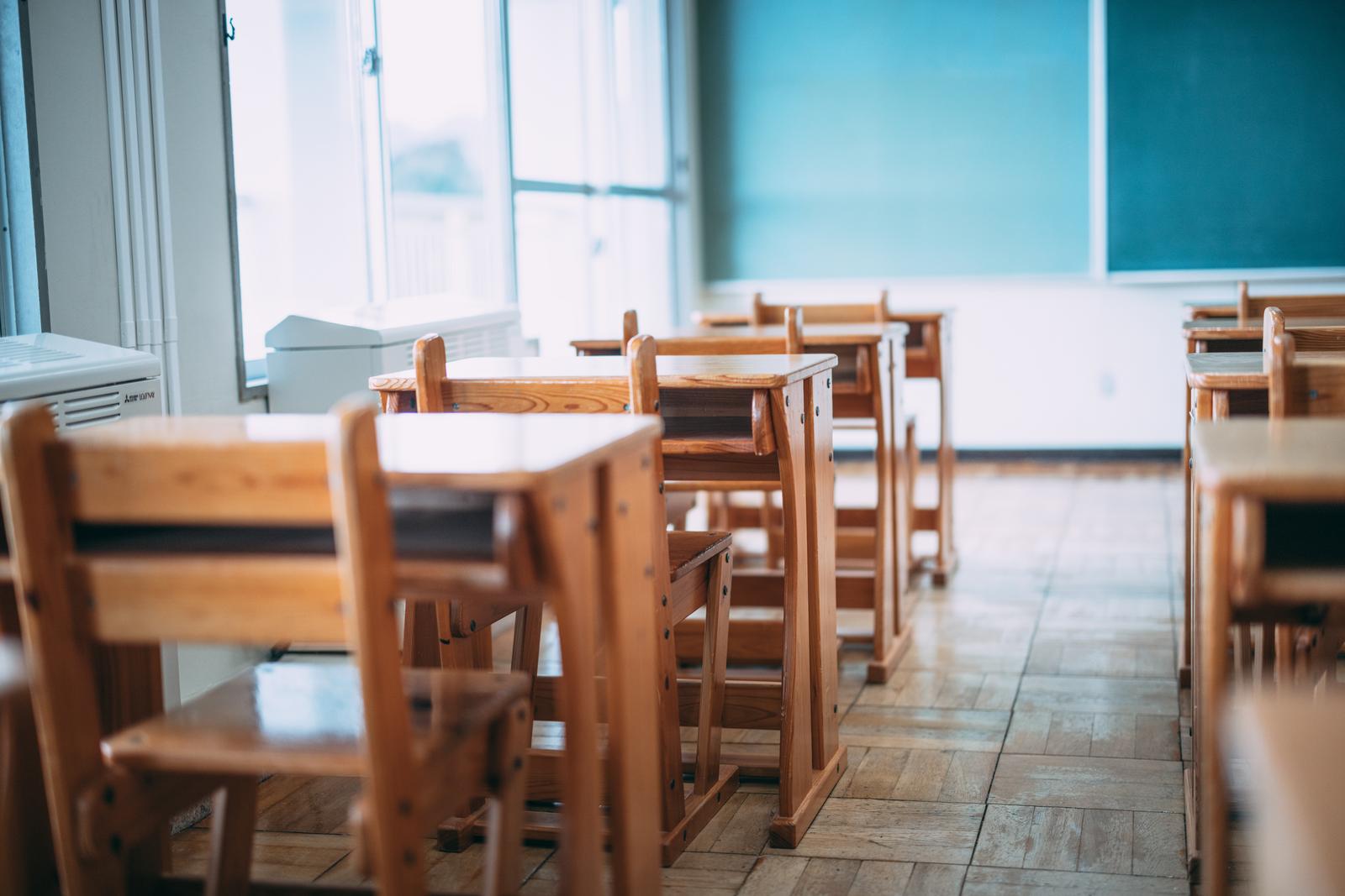 木製の机と椅子が置かれた明るい学校教室