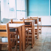 木製の学校の机と椅子が並ぶ教室、窓からの採光が明るい学習環境の写真