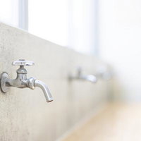 廃校舎に残る学校の水飲み場の蛇口と経年劣化したコンクリート壁の写真