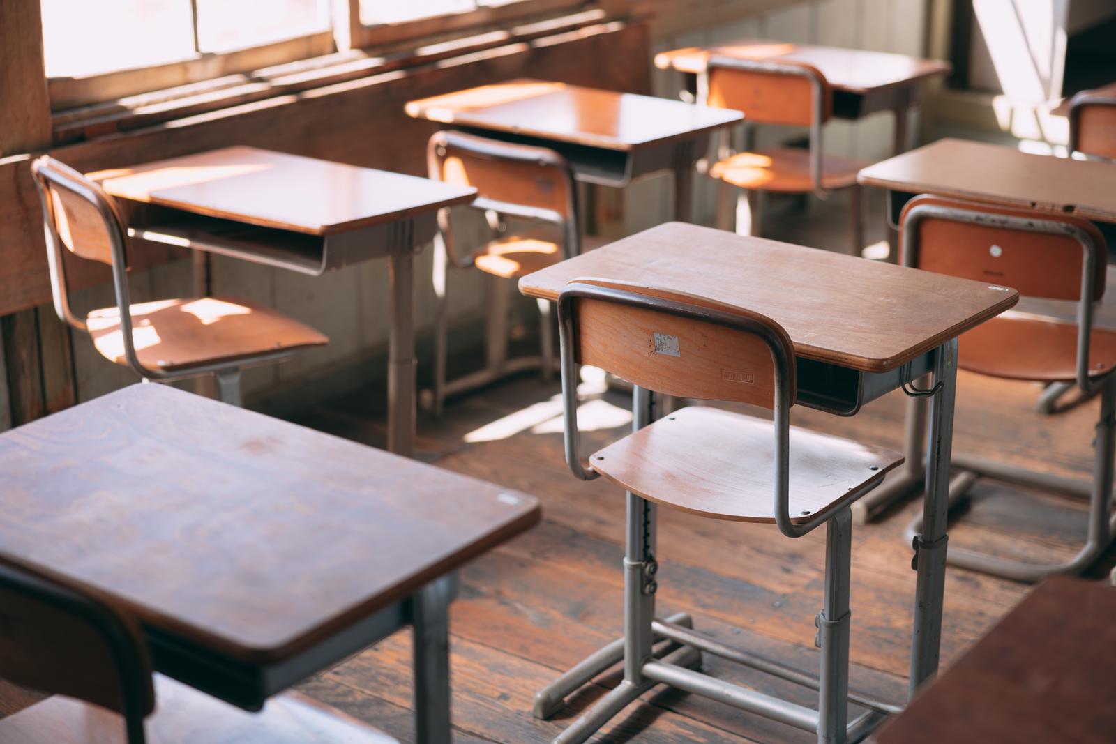 木製の学習机と椅子が並ぶ教室。窓から光が差し込んでいる