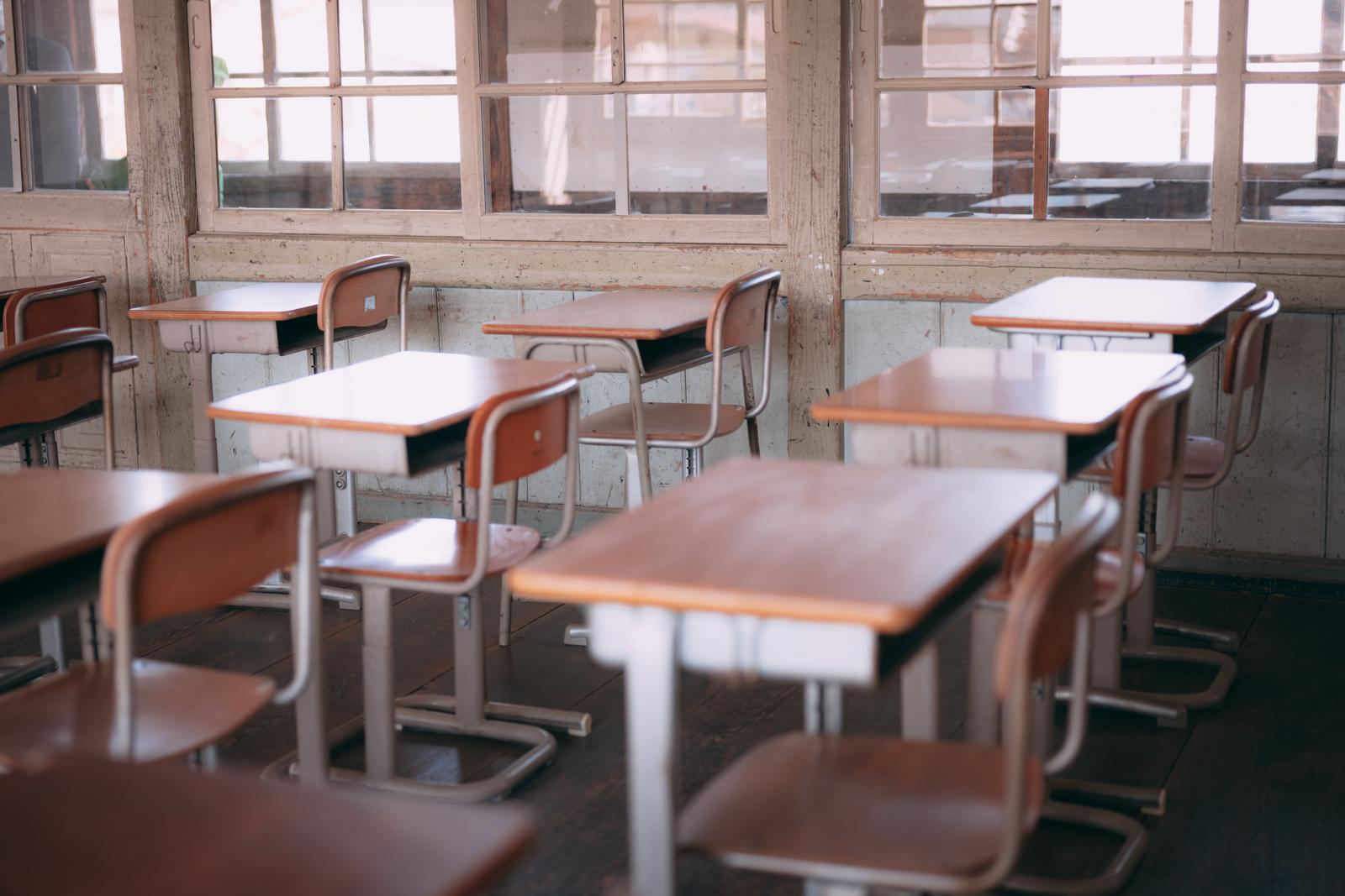 古い校舎の教室に整列した茶色い学習机と椅子
