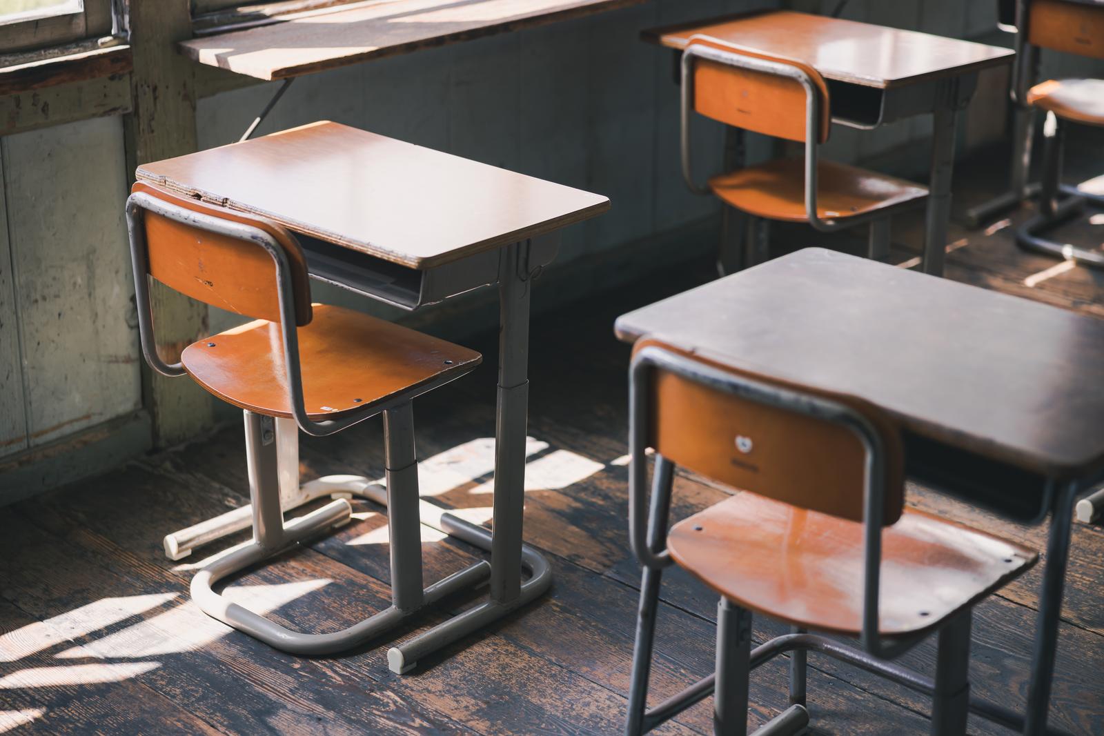オレンジ色の椅子が付いた学習机が複数並ぶ教室の光景