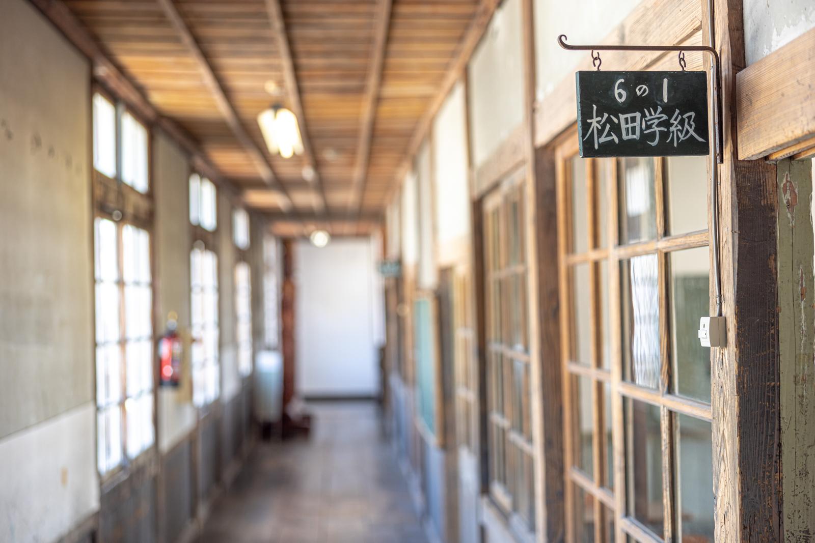 昭和の木造校舎の放課後の廊下、教室ドアに6の1松田学級の看板が掛かる
