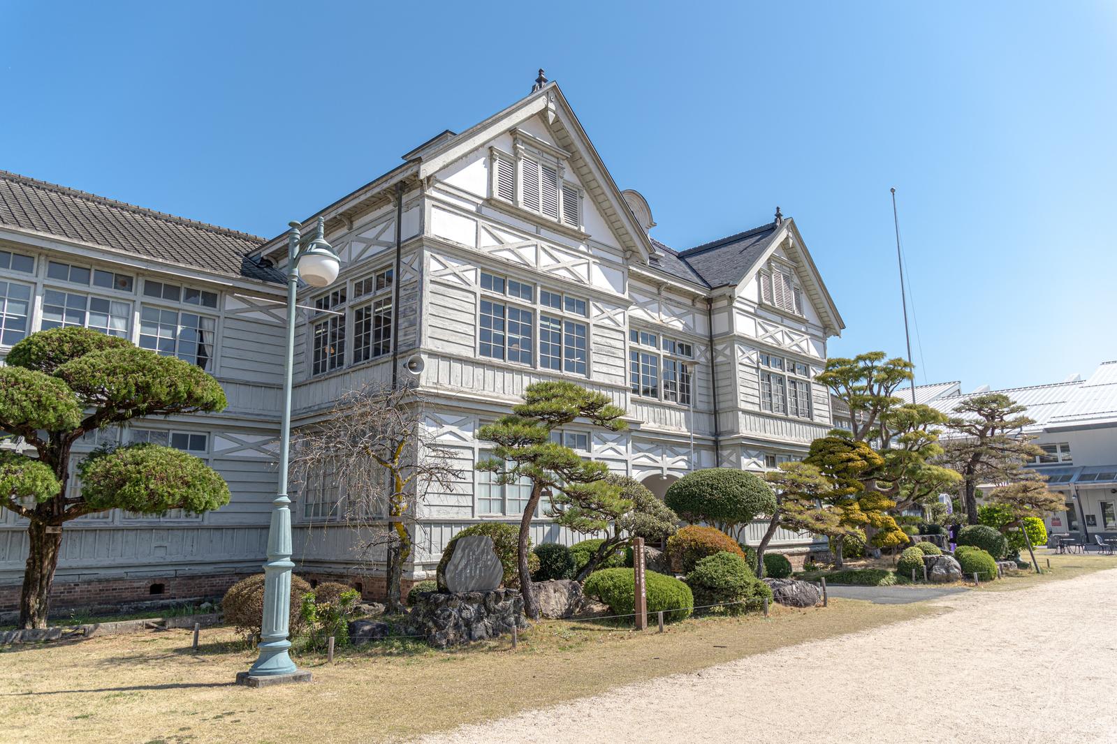 白い洋館風の木造校舎とレトロな街灯がある旧遷喬尋常小学校の外観