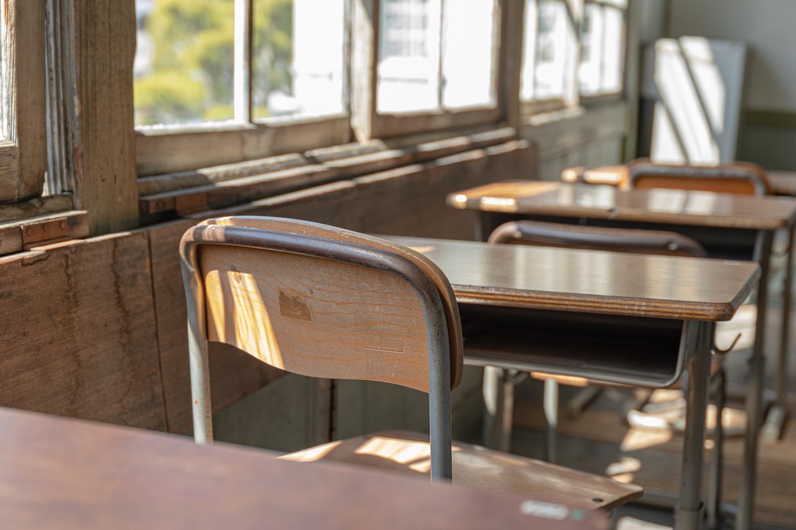 窓から光が差し込む教室の中に整列した木製の学習机と椅子