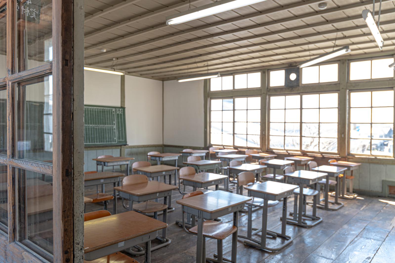 旧遷喬尋常小学校の教室に並ぶ学習机と学習椅子、窓からの光が差し込む