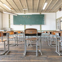 窓を望む旧遷喬尋常小学校の教室と学習机・黒板の写真