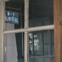 窓ガラス越しに見る学級表示板と校舎の教室札の写真