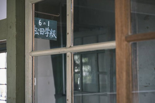 窓ガラス越しに見る学級表示板と校舎の教室札