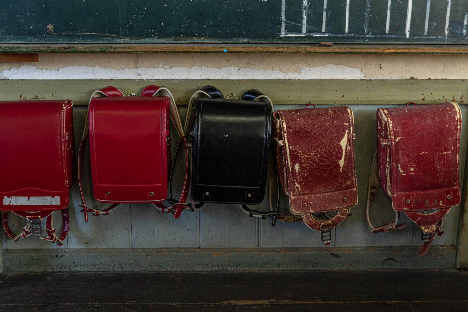 校舎の壁に掛けられた赤と黒の古いランドセル複数個