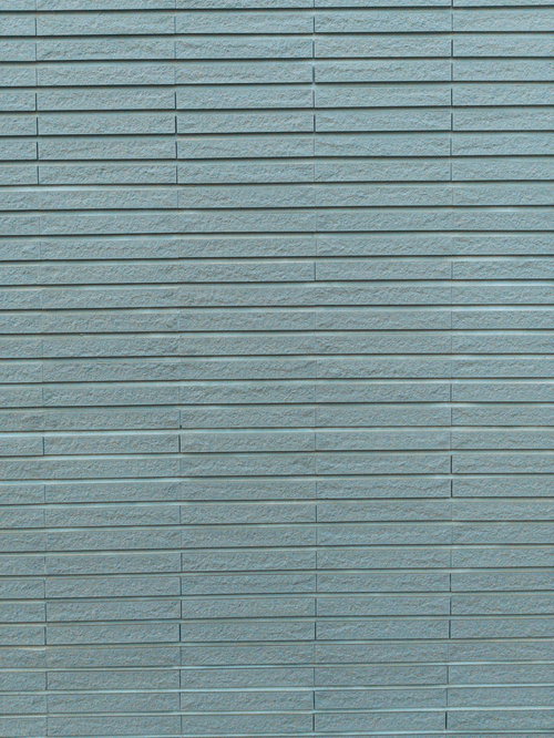 グレー色の建材タイルが水平に並ぶ継ぎ目が粗い外壁
