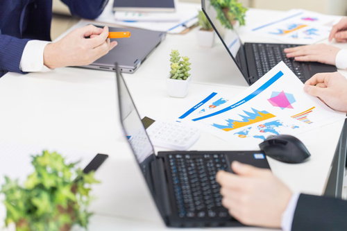 紙の資料とパソコンを用いて会議をするビジネスパーソン