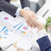 テーブルの資料前で握手を交わすビジネスマンの写真