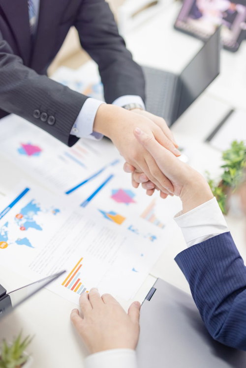 テーブルの資料前で握手を交わすビジネスマン