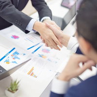 成約後にテーブルを前に握手を交わすビジネスパーソンの写真