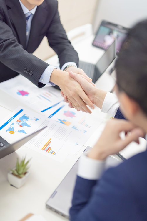 成約後にテーブルを前に握手を交わすビジネスパーソン