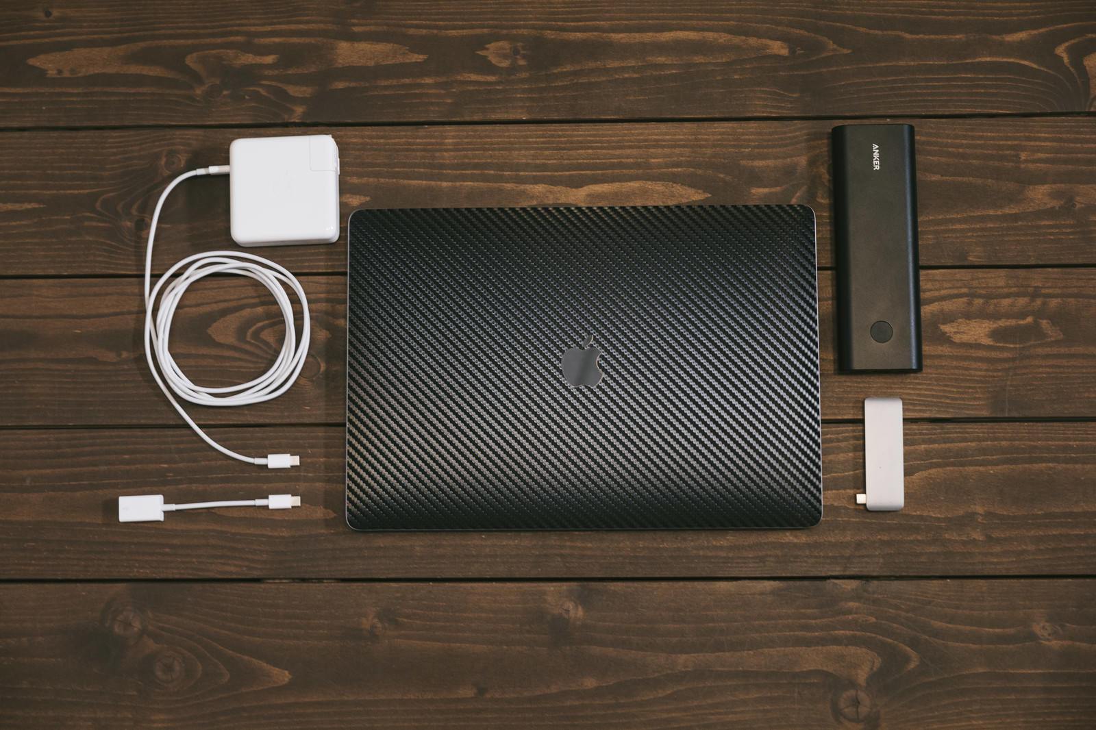 木目テーブルにMacBookと充電器・モバイルバッテリーを並べた俯瞰