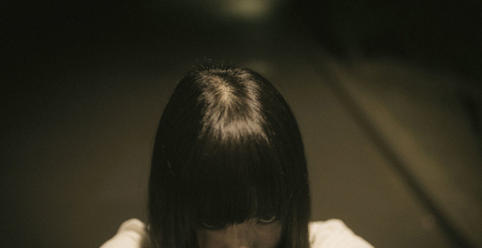 暗い室内で髪で顔を隠しうつむく女性［モデル：さとうゆい］