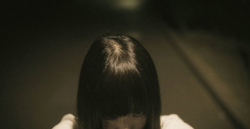 暗がりで髪で顔を隠し恨みを込める女性の不気味な表情