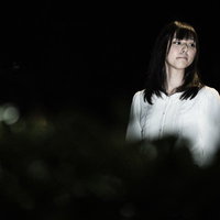 不気味な夜道を怖がりながら歩く女性と懐中電灯の光の写真