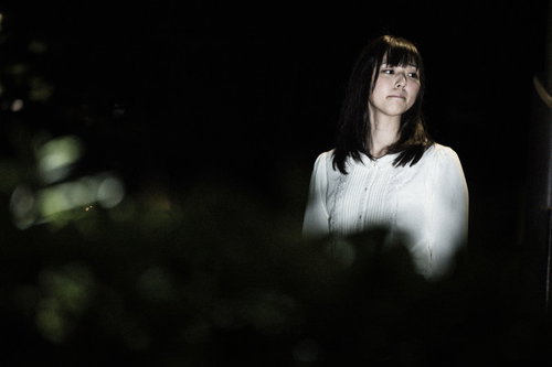 不気味な夜道を怖がりながら歩く女性と懐中電灯の光