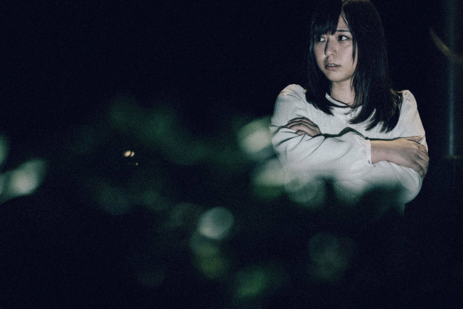 薄暗い夜間で警戒した表情を見せる白いTシャツの女性［モデル：さとうゆい］
