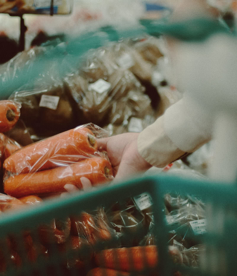 小高ストアの野菜コーナーで人参の袋を手に取る女性