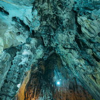 備中鐘乳穴の天井から連なる巨大な鍾乳石と青緑色の石灰岩層の写真