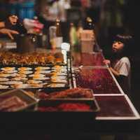 屋台の鉄板で焼くお好み焼きと少女の調理風景の写真