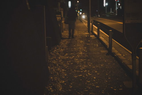 深夜の帰宅、街灯の下を歩く人影、夜道の薄暗さ