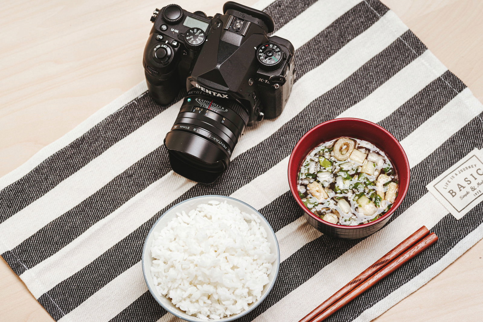 黒いストライプの布の上に置かれた一眼レフカメラと和食の朝食セット