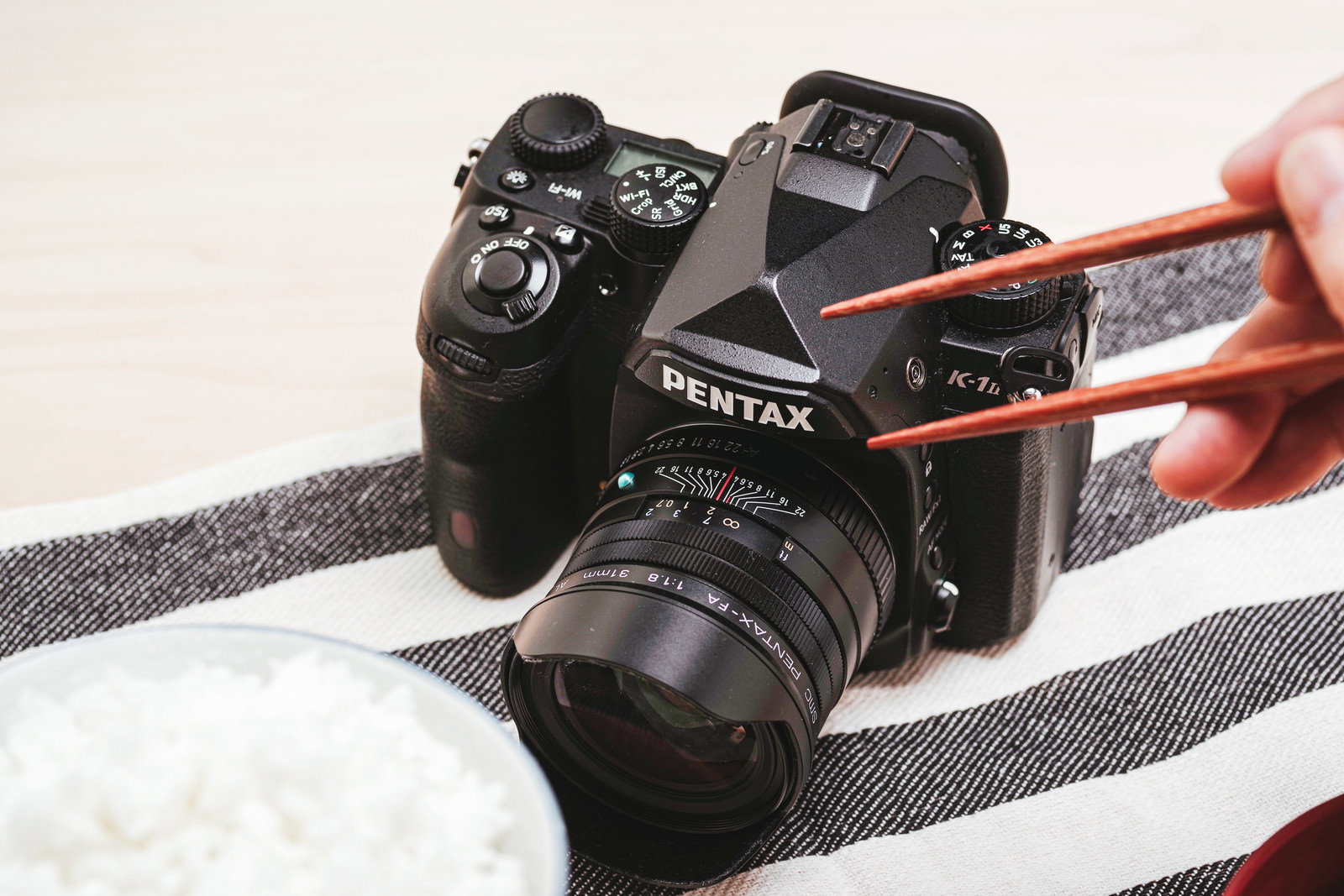 PENTAXの一眼レフカメラと和食の朝食がテーブルに並んでいる様子