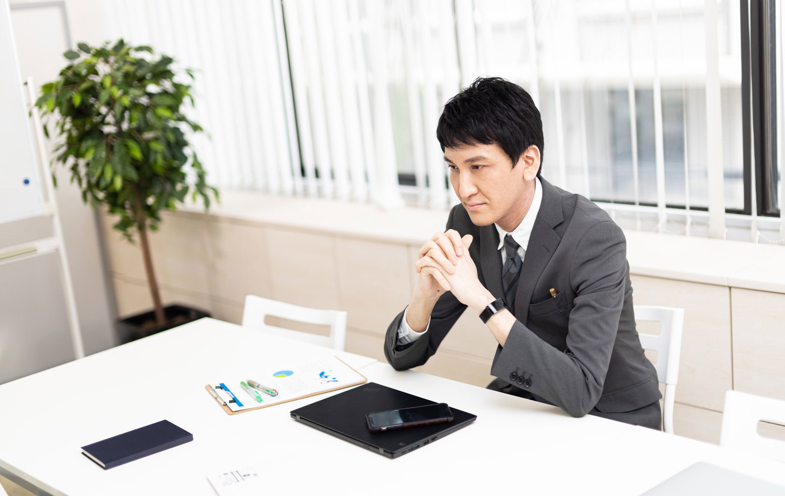 会議室で手を組み考え込むスーツ姿の男性［モデル：ACE］
