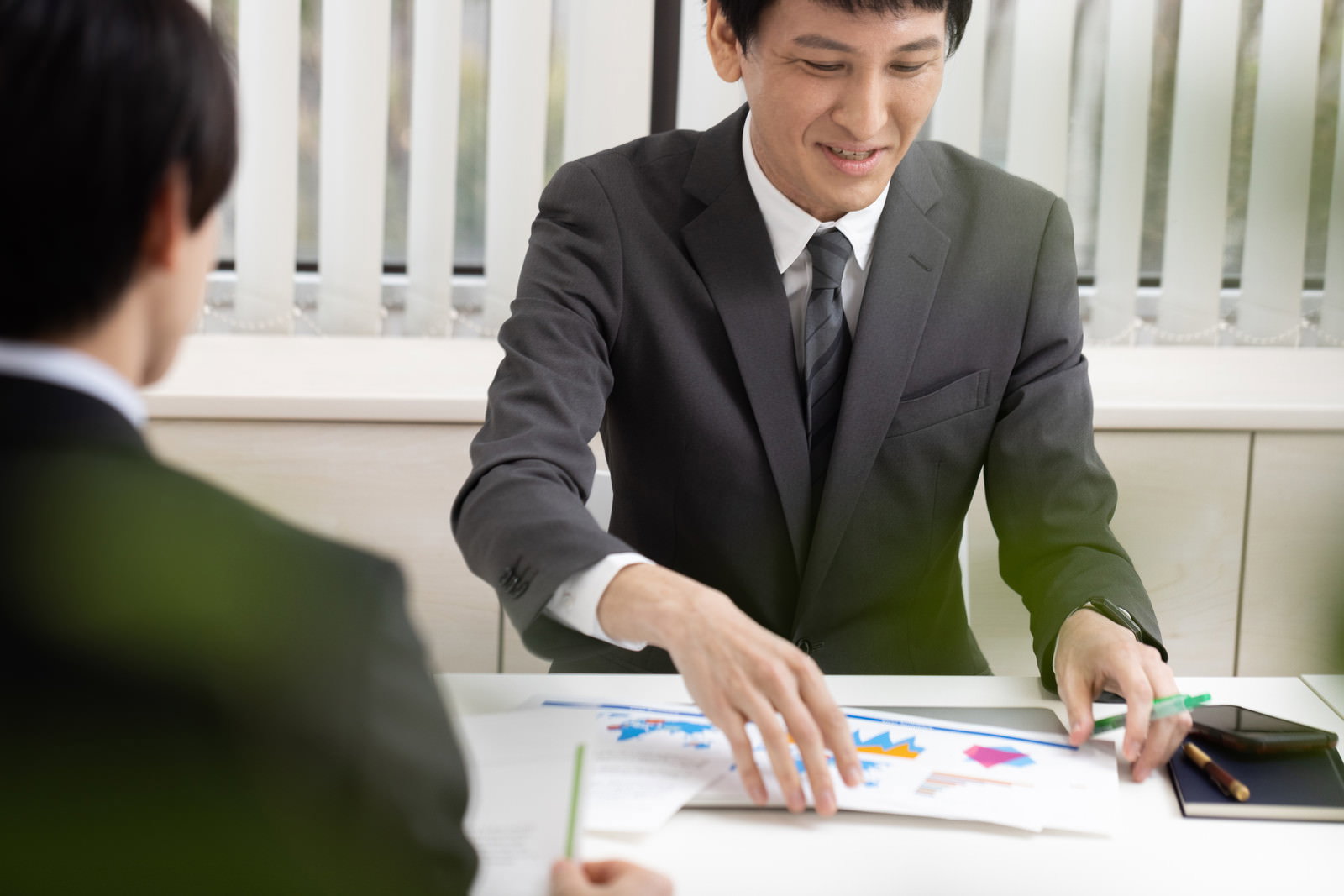会議室でプリントした資料を手に取るスーツ姿の営業担当者［モデル：ACE］